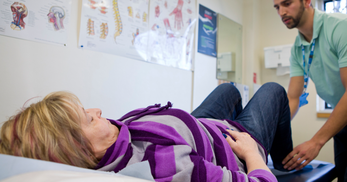 Physiotherapist Holding The Ankles Of A Patient Whilst They Lie On A Medical Bed