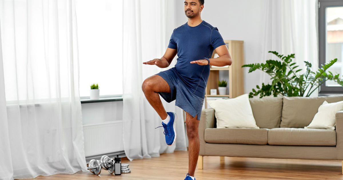 Young asian man running on the spot wearing a t-shirt and shorts in their living room on a wooden floor.