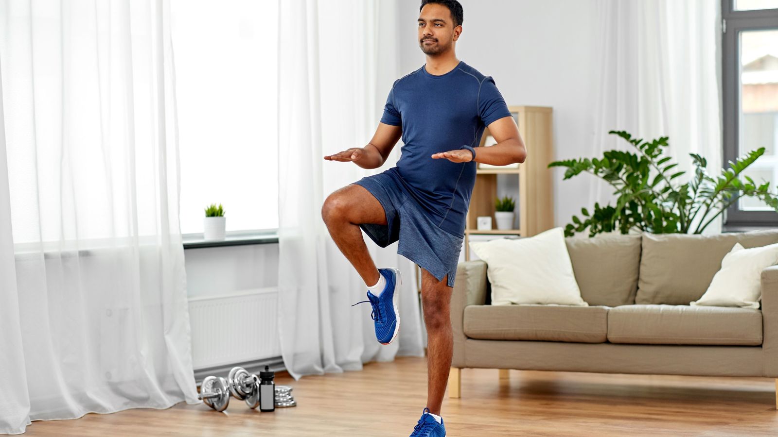 Young asian man running on the spot wearing a t-shirt and shorts in their living room on a wooden floor.